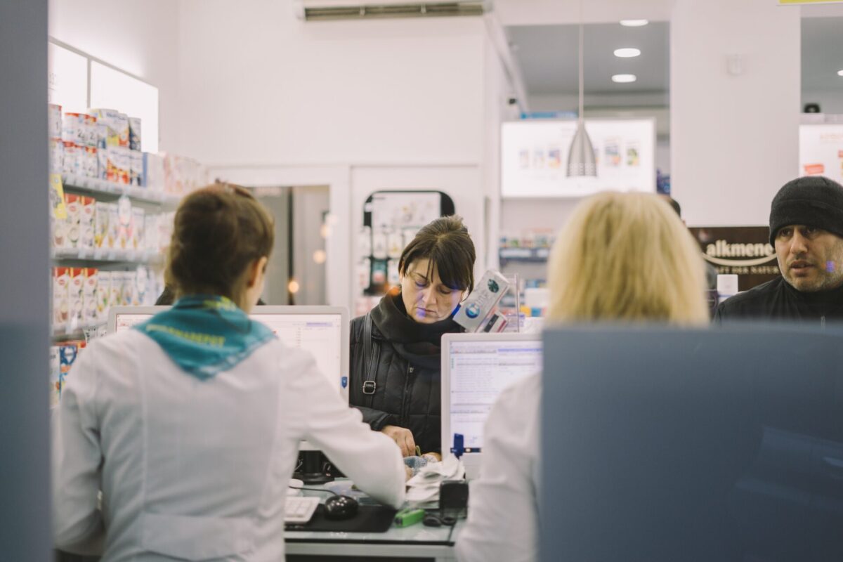 Picture of two customers at a pharmacy with two staff serving them.